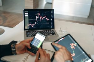Hands using digital devices for financial analysis at a modern desk setup.